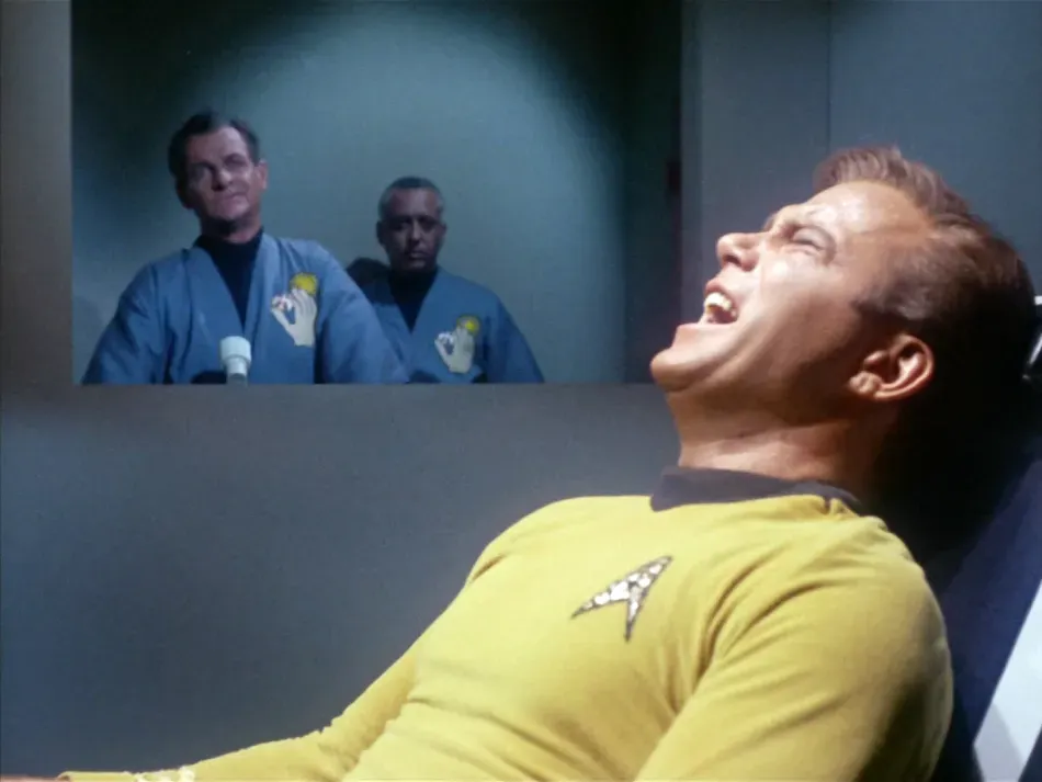 Kirk screaming while two men in blue uniforms look on.